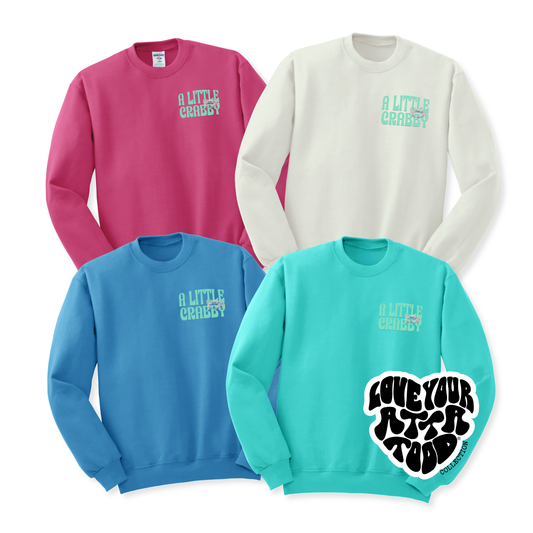 Four sweatshirts in pink, white, blue, and teal with text and graphics on the front. A little crabby w Text with a crab