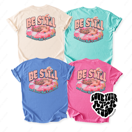 Four colorful Comfort Colors® t-shirts with a pink flamingo floar that says be still and know that I am god on a white background. colors blue, pink, ivory and minty blue