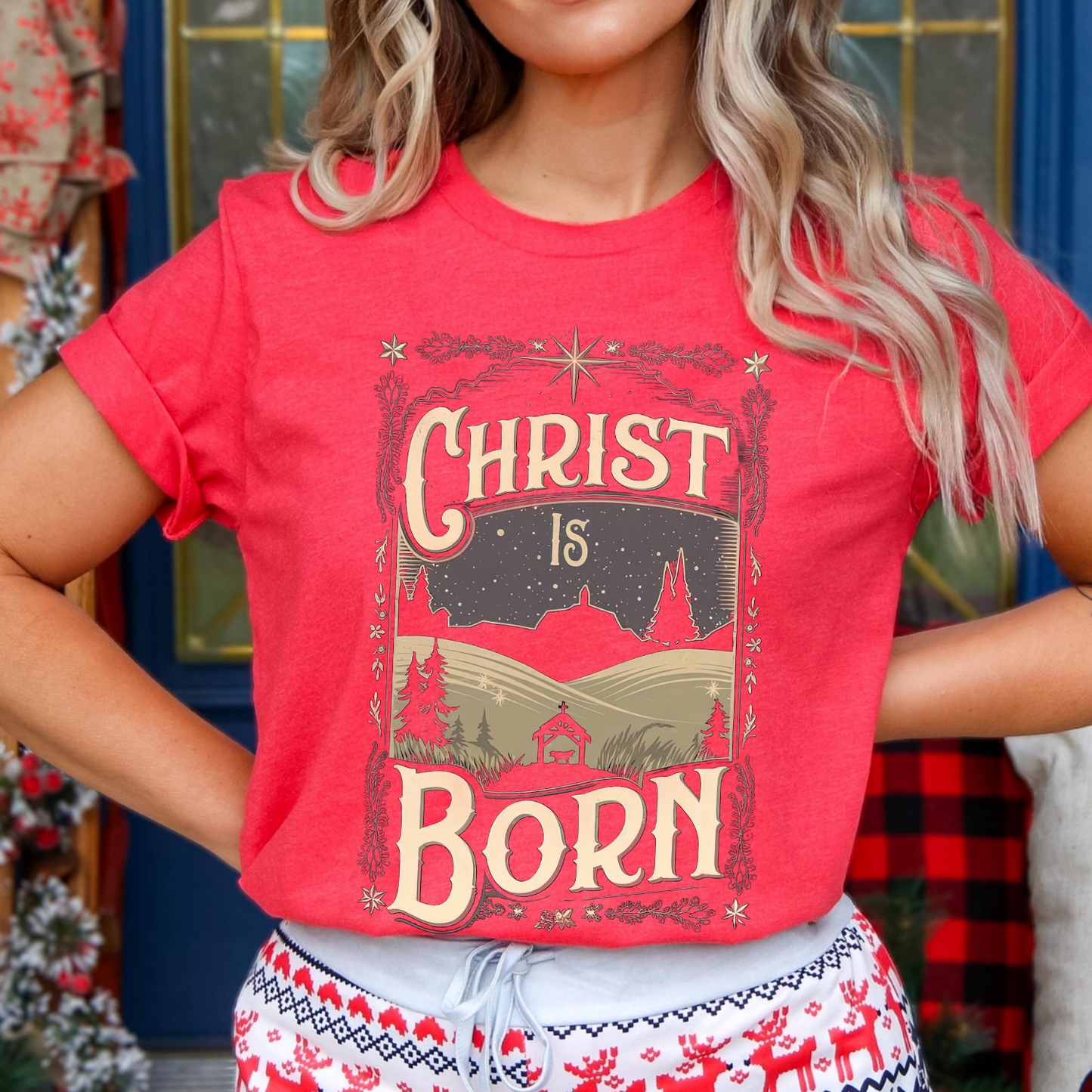Person wearing a red t-shirt with 'Christ is Born' design in front of a decorated Christmas tree.