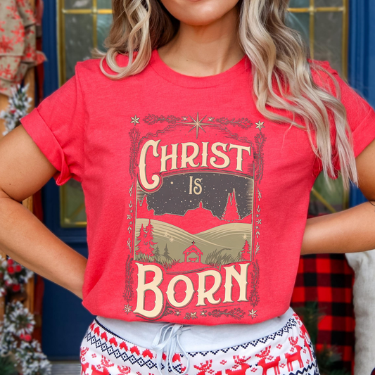 Person wearing a red t-shirt with 'Christ is Born' design in front of a decorated Christmas tree.