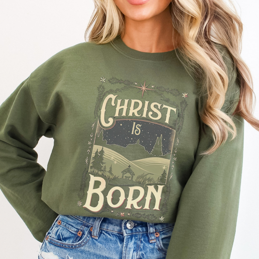 Person wearing a green sweatshirt with 'Christ is Born' text and landscape design.