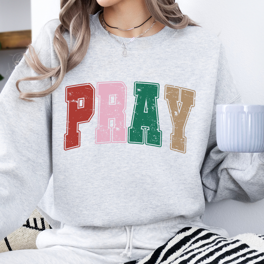 Person wearing a Ash gray sweatshirt with the words PRAY across the chest with the colors red, pink, green, tan