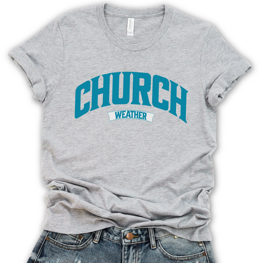 A gray unisex graphic t-shirt with the text 'CHURCH' in blue and 'weather' in a smaller font, displayed on a flat surface with casual clothing.
