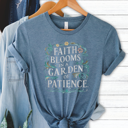 A blue graphic t-shirt with the text 'FAITH BLOOMS IN A GARDEN OF PATIENCE' printed on the front, displayed on a hanger.