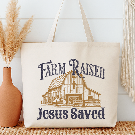 Beige tote bag with 'Farm Raised Jesus Saved' text and barn illustration next to a vase with dried plants.