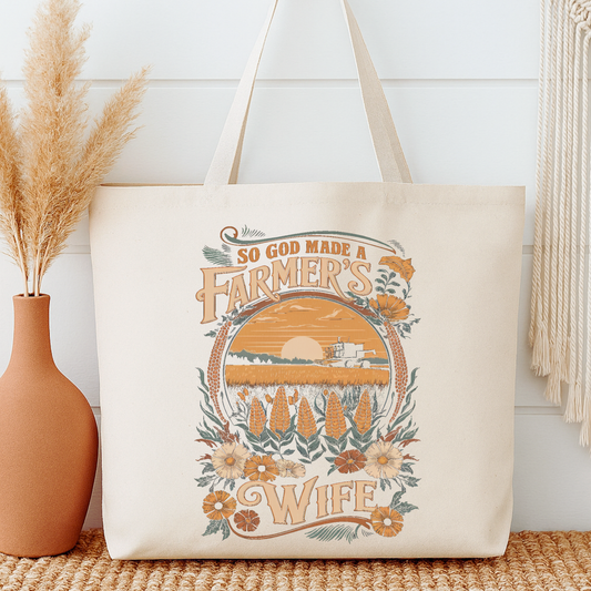 Tote bag with 'So God Made a Farmer's Wife' design next to a vase with dried plants on a wooden surface.