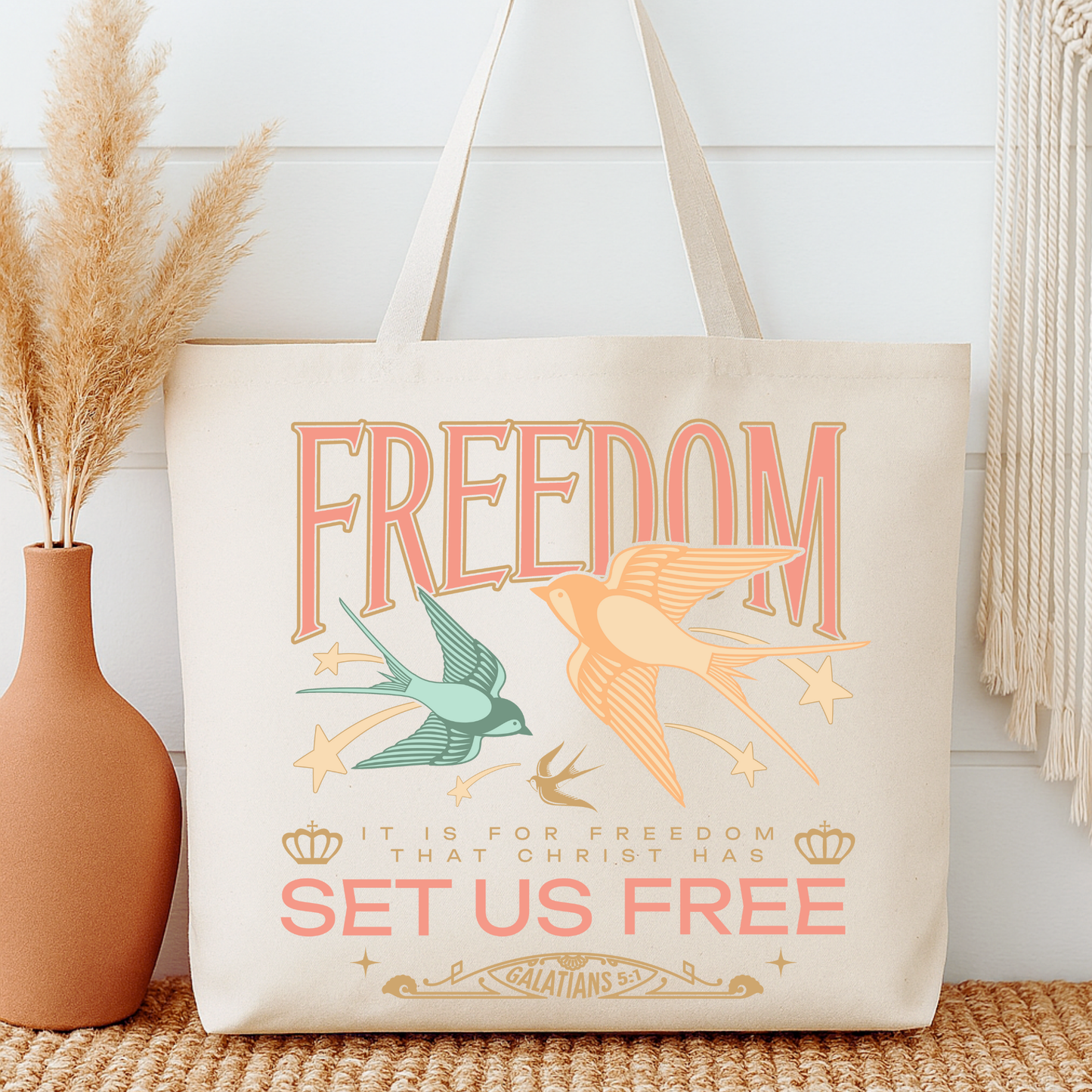 Tote bag with 'Freedom' design featuring birds and text, next to a vase with dried plants.