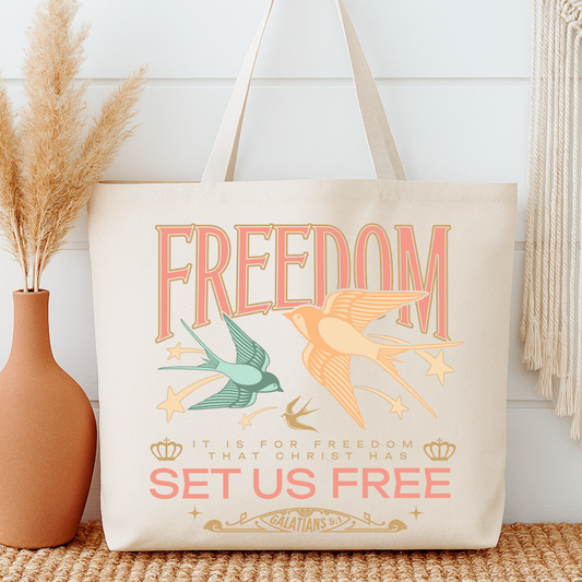 Tote bag with 'Freedom' design featuring birds and text, next to a vase with dried plants.