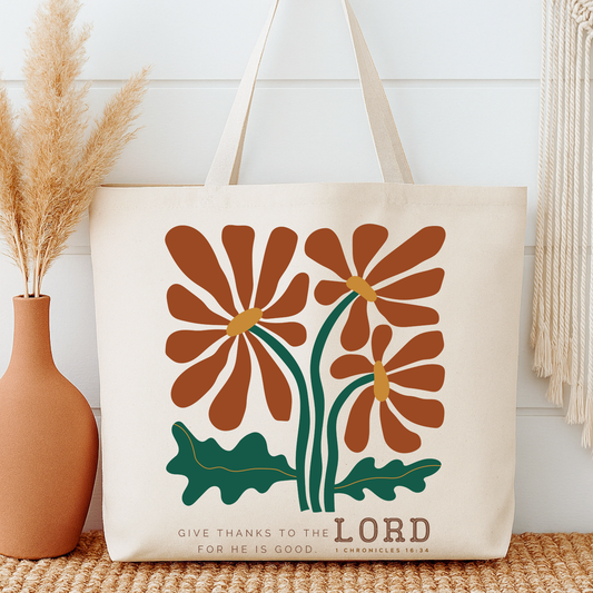 Tote bag with floral design and 'Give thanks to the Lord' text next to a vase on a wooden surface.