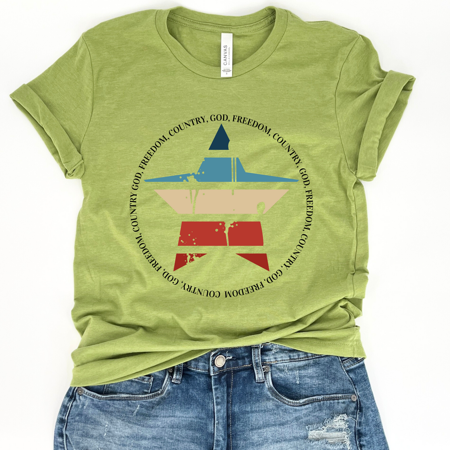 A green unisex graphic t-shirt with a text and symbol design that includes the colors of the American flag and the phrase 'God Freedom Country'. The shirt is presented alongside a pair of blue denim shorts.