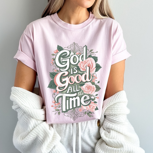 Person wearing a pink t-shirt with 'God is Good All the Time' text and floral design.