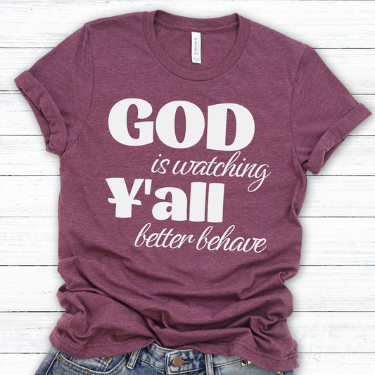 A maroon-colored graphic t-shirt with the text 'GOD is watching Y'all better behave' printed in white.