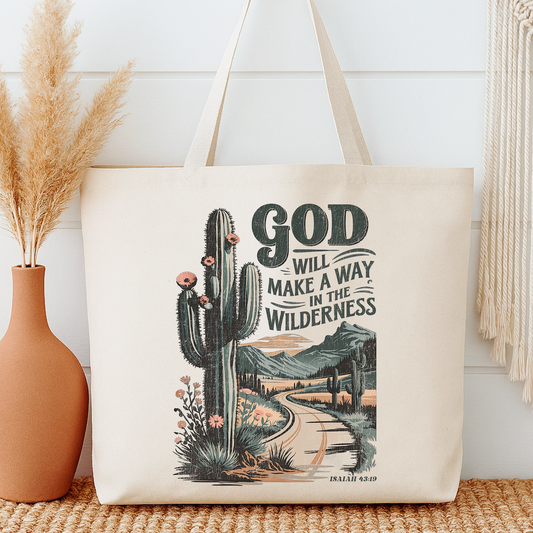 Tote bag with cactus design and 'God will make a way in the wilderness' text next to a vase.
