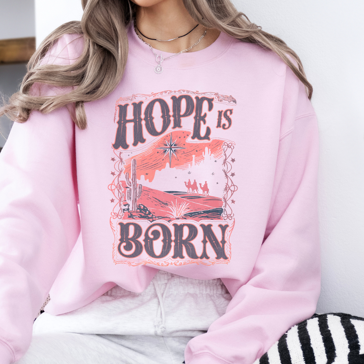Person wearing a pink sweatshirt with 'Hope is Born' graphic design.