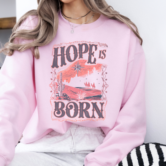 Person wearing a pink sweatshirt with 'Hope is Born' graphic design.
