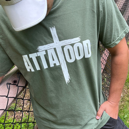 A man wearing comfort color moss green t-shirt with ATTA TOOD in the middle with a large rustic cross in the center