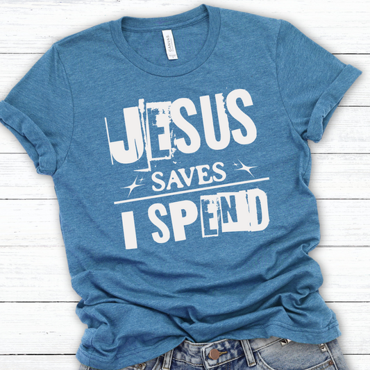 A blue graphic t-shirt with the text 'JESUS SAVES I SPEND' printed on the front, displayed on a casual fit mannequin with denim shorts.