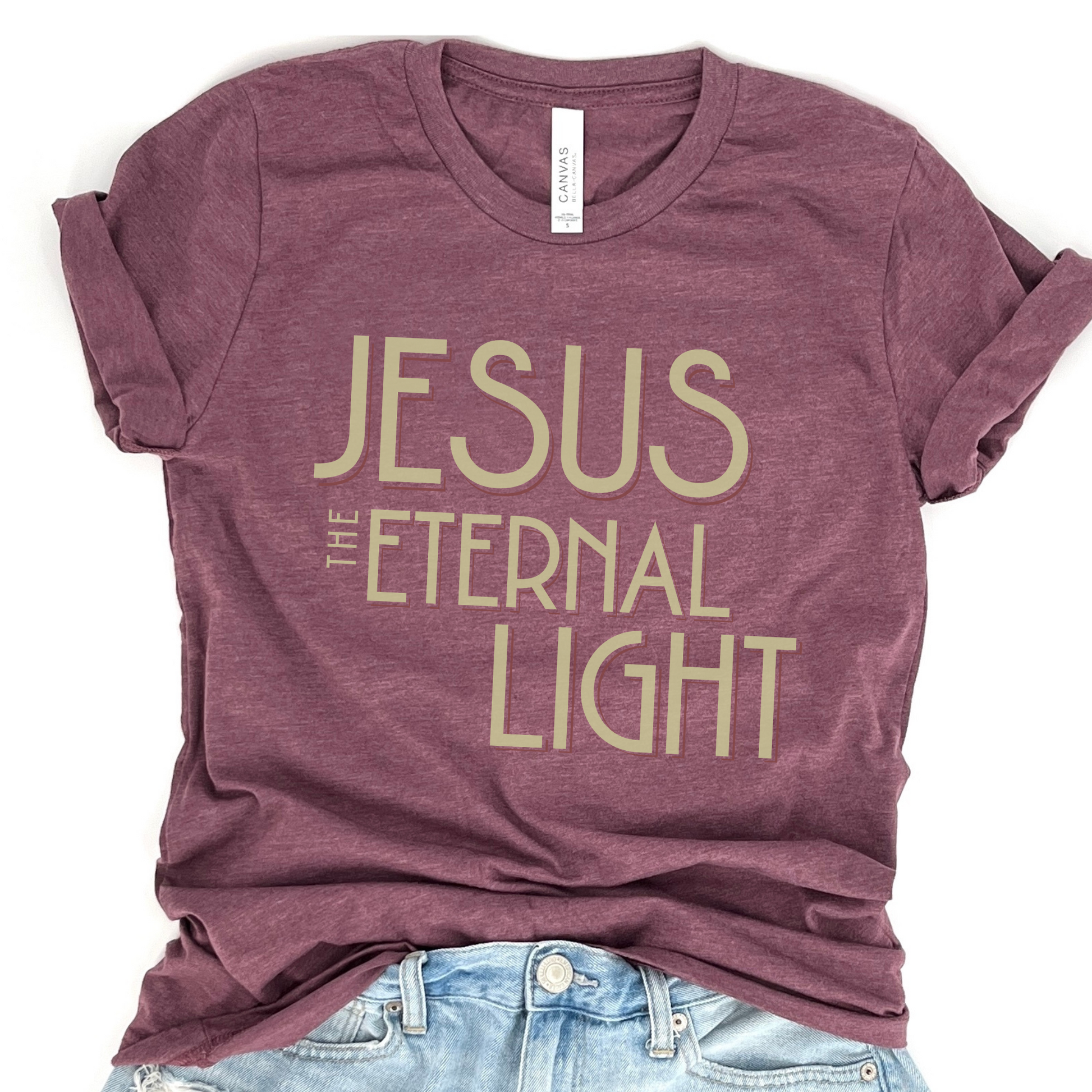 A maroon-colored graphic t-shirt with the text 'JESUS THE ETERNAL LIGHT' printed in gold.
