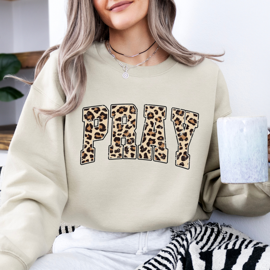 A person wearing a beige sweatshirt with a leopard print and the text 'PRAY' printed on the front.