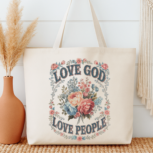 Beige tote bag with 'Love God Love People' text and floral design next to a vase with dried plants.
