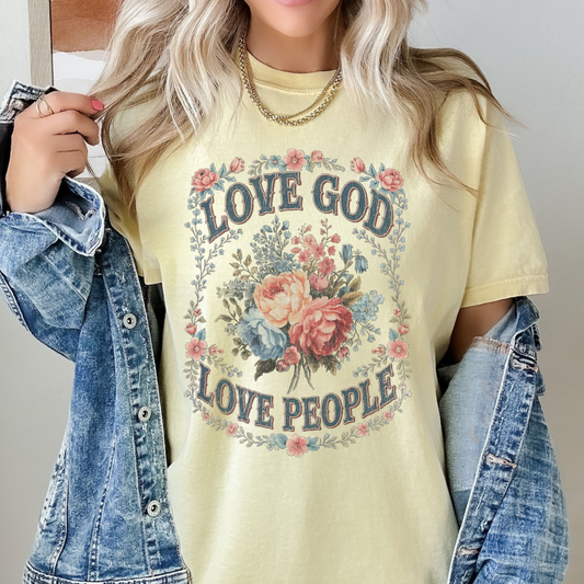 Person wearing a yellow t-shirt with 'Love God Love People' text and floral design.