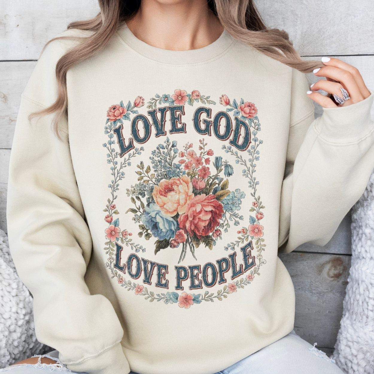 Person wearing a cream sweatshirt with 'Love God Love People' text and floral design.