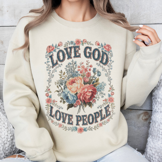 Person wearing a cream sweatshirt with 'Love God Love People' text and floral design.