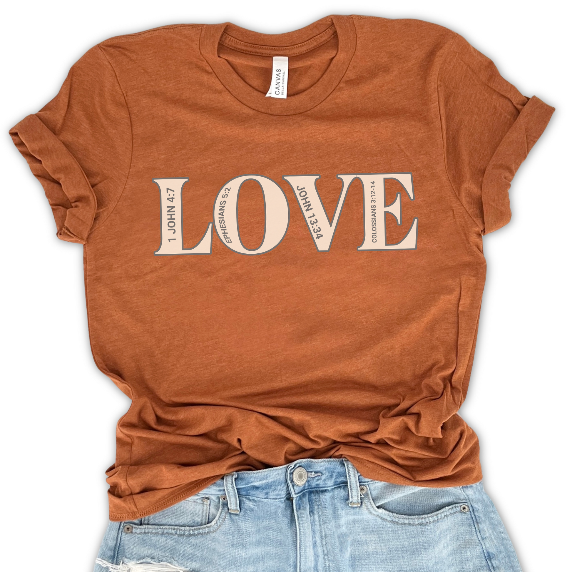 A brown graphic t-shirt with the word 'LOVE' printed in white on the front, displayed on a flat surface with casual blue jeans next to it.