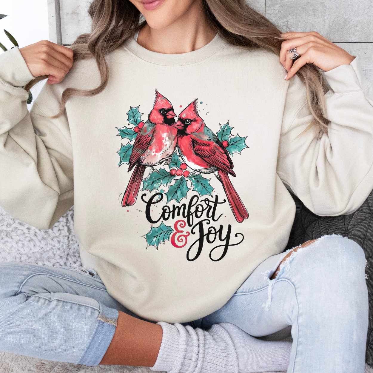 Person wearing a cream sweatshirt with cardinal design and 'Comfort & Joy' text.