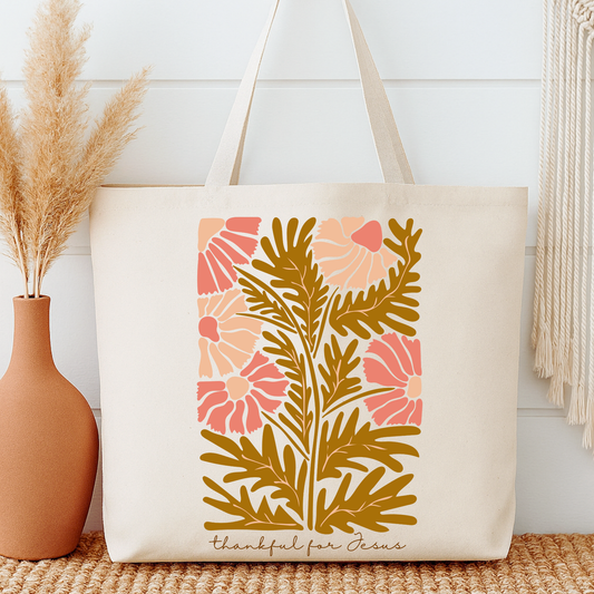 Tote bag with floral design and text next to a vase on a wooden surface.  Thankful for Jesus