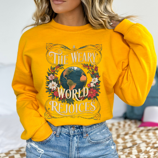 Person wearing a yellow sweatshirt with a graphic design and text.  The weary world rejoices with poinsettias and a graphic of the world in the center