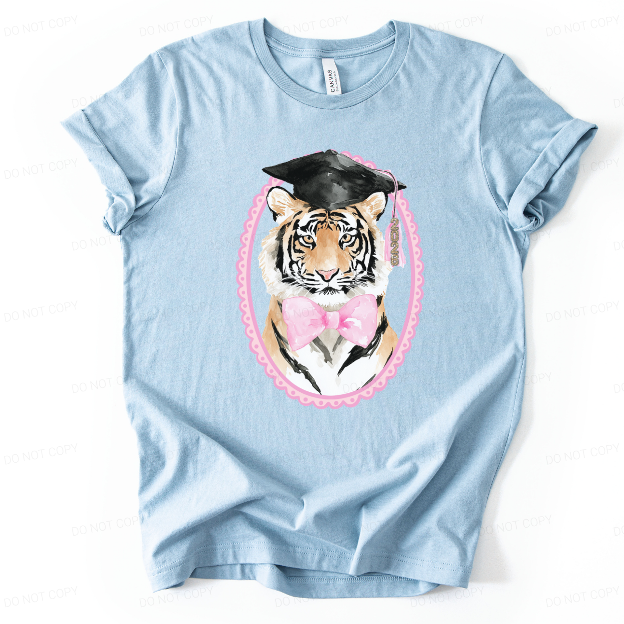 Graduation 2026 mascot themed graphic t shirt. The design features a detailed tiger portrait wearing a black graduation cap with a 2026 tassel, accented with a soft pink bow and framed in a decorative oval border. The combination of mascot styling and feminine pink accents creates a strong senior year statement with clear Class of 2026 visibility.