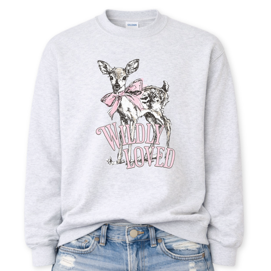 Ash gray Bold Christian graphic on a Gildan crewneck sweatshirt. The design features a fawn with soft brown detailing and a large pink bow, paired with the phrase “Wildly Loved” in blush vintage-style lettering.