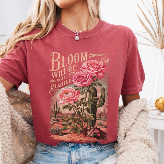 Person wearing a red t-shirt with floral and cactus design and 'Bloom Where You Are Planted' text.