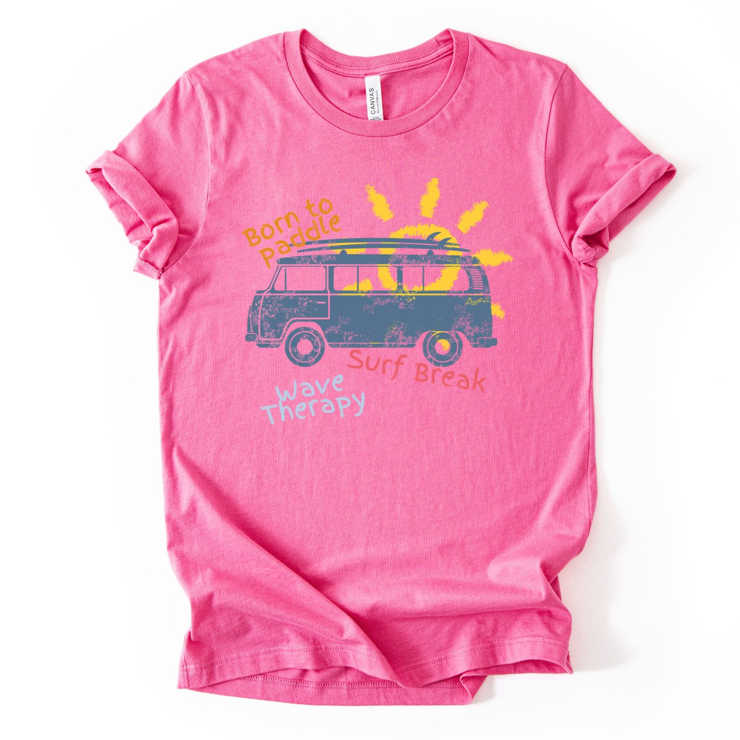 Summer beach graphic on a soft unisex heather charity pink graphic tee. The design features a vintage surf van illustration with a surfboard on top and a bright sun rising behind the vehicle. Playful coastal phrases including Born to Paddle, Surf Break, and Wave Therapy surround the artwork, creating a relaxed surf and beach lifestyle graphic that captures the feeling of ocean days and summer travel.