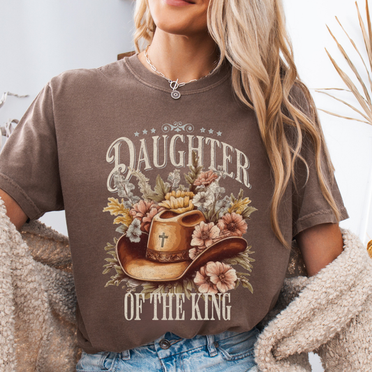 Person wearing a brown t-shirt with 'Daughter of the King' graphic design.