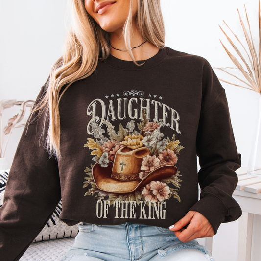 Person wearing a chocolate brown sweatshirt with 'Daughter of the King' design. Graphic is of a cowboy hat with a cross nestled in flowers