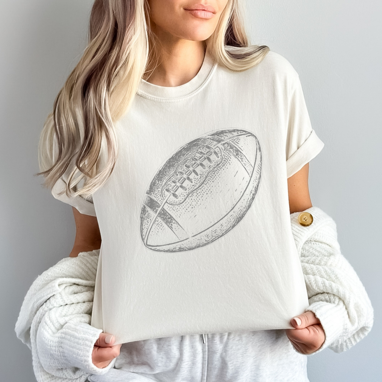 Person wearing a white t-shirt with a football graphic on a plain background