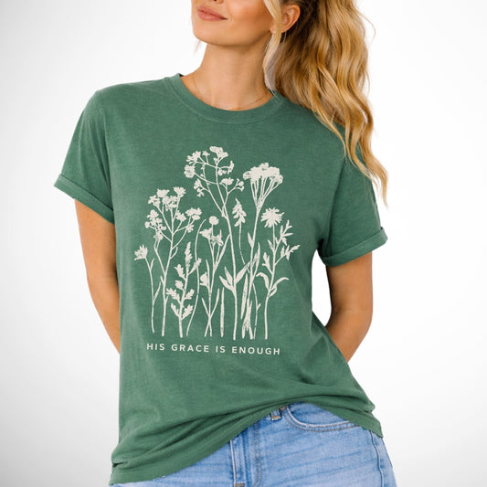 Woman wearing a green t-shirt with floral design and text on a white background that says His Grace is enought