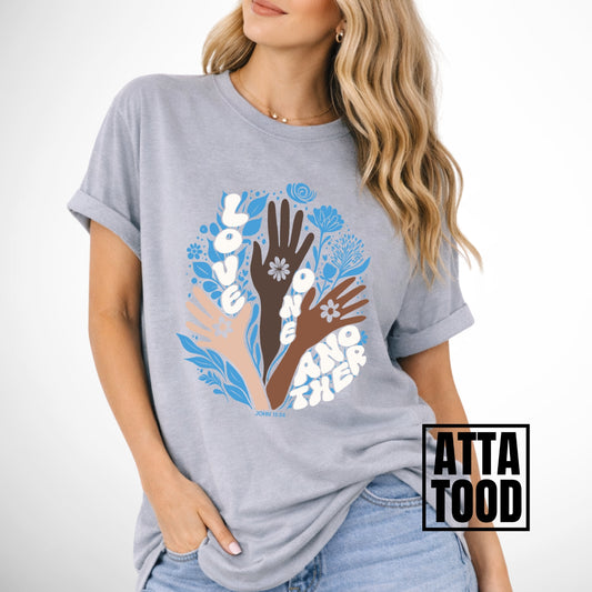 Person wearing a gray t-shirt with a colorful graphic of hands and flowers on a white background. John 13 Love One Another Comfort Colors Graphic Tee