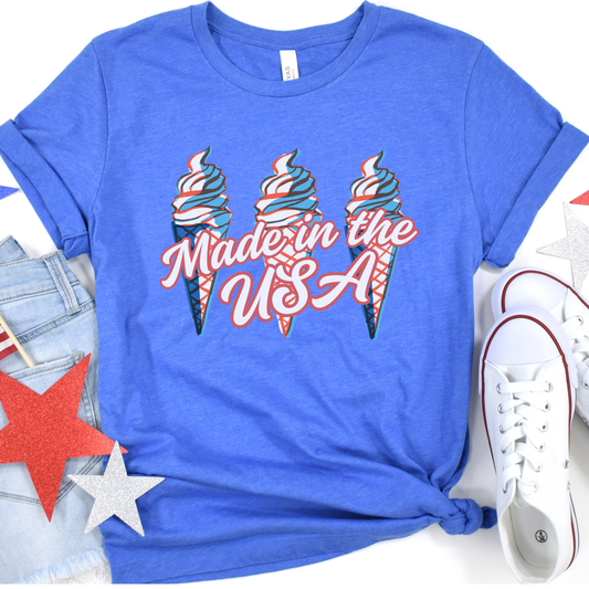 A blue t-shirt with 'Made in the USA' graphic featuring three ice cream cones in red, white, and blue, placed on a surface with denim, white sneakers, and decorative stars.