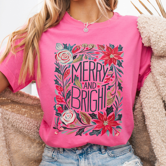 Person wearing a pink t-shirt with floral design and 'Merry and Bright' text.