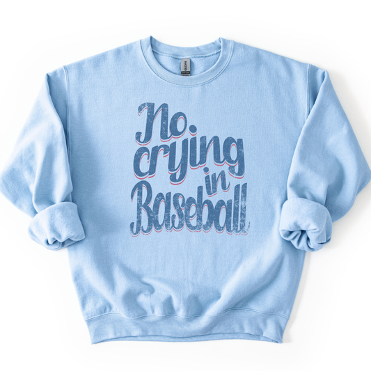 Light blue crewneck sweatshirt featuring distressed retro script text reading “No Crying in Baseball,” styled flat with sleeves scrunched
