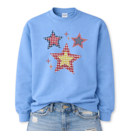 Patriotic patchwork star graphic on a blue sweatshirt. The design features a cluster of illustrated stars in varied sizes, each filled with classic red, white, and blue gingham-style patterns, including plaid and check textures. Small accent sparkles add movement while the layered patchwork look gives the graphic a cozy, Americana feel. A versatile patriotic design ideal for Fourth of July, summer events, and seasonal USA collections.