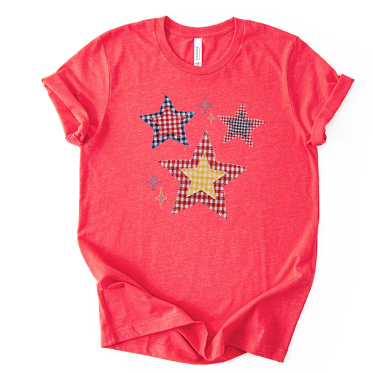 Patriotic Americana star graphic on a red t-shirt. The design features illustrated patchwork stars arranged in a playful cluster, using red, white, and blue gingham-style patterns with subtle texture and stitching detail. Small accent stars add movement and balance around the main shapes. The overall look feels classic, cheerful, and vintage-inspired, making it ideal for Fourth of July, summer Americana collections, and everyday patriotic wear.