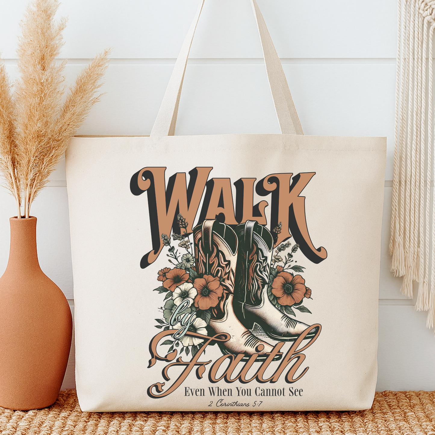 Tote bag with 'Walk by Faith' design featuring boots and flowers, placed on a surface with decorative elements.