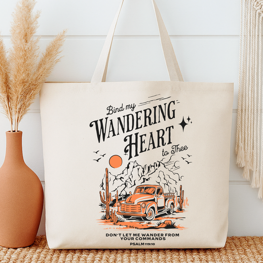 Tote bag with a truck and cactus design, text 'Bind my wandering heart to thee', next to a vase with dried plants.