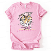 Graduation 2026 graphic t-shirt. The design features a detailed tiger illustration centered on the front, wearing a pink mortarboard cap with tassel and a large pink bow at the neck. Below the illustration, Twenty-Twenty-Six is printed in light lettering with a pink script graduate accent