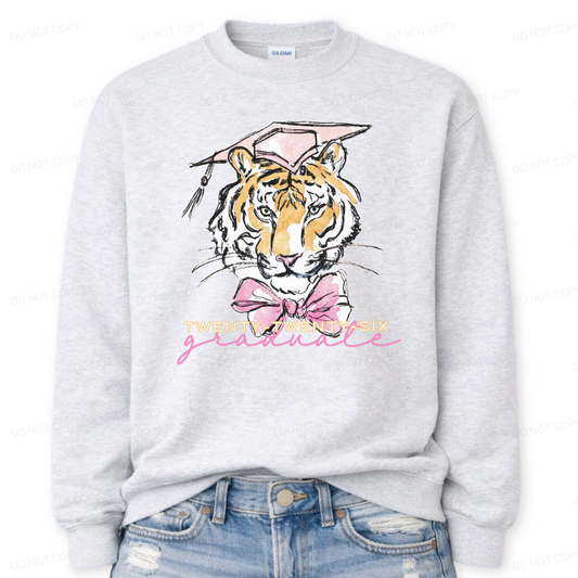 Graduation 2026 tiger graphic ash crewneck sweatshirt. The design features a detailed tiger face illustration wearing a pink graduation cap, finished with a soft pink bow at the neckline. Twenty Twenty Six graduate lettering sits below the artwork, creating a clear Class of 2026 message with a school spirit mascot look that works for both high school and college graduation customers.