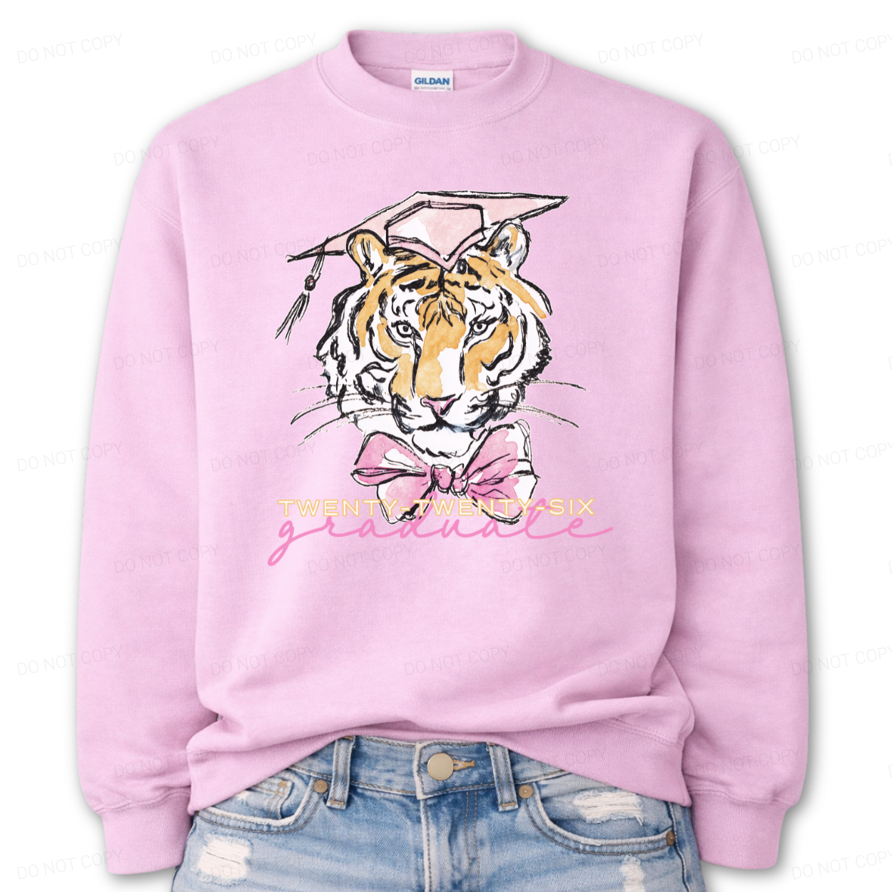 Graduation 2026 tiger graphic pink crewneck sweatshirt. The design features a detailed tiger face illustration wearing a pink graduation cap, finished with a soft pink bow at the neckline. Twenty Twenty Six graduate lettering sits below the artwork, creating a clear Class of 2026 message with a school spirit mascot look that works for both high school and college graduation customers.